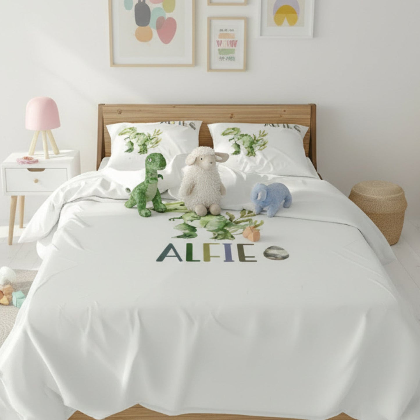 Children's bedroom with a bed featuring a white comforter with embroidered name 'ALFIE', surrounded by stuffed animals and decor.